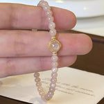 Pink beaded bracelet with a gold clasp held on a hand against a neutral background
