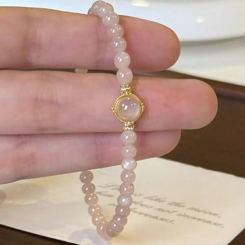 Pink beaded bracelet with a gold clasp held on a hand against a neutral background