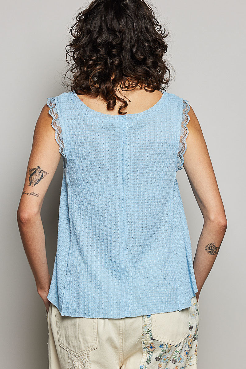 Person wearing a light blue sleeveless top with lace trim on a plain background