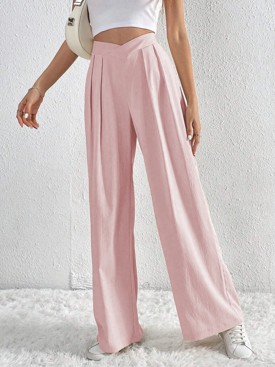 Person wearing light pink wide-leg pants with a white top and sneakers on a white background