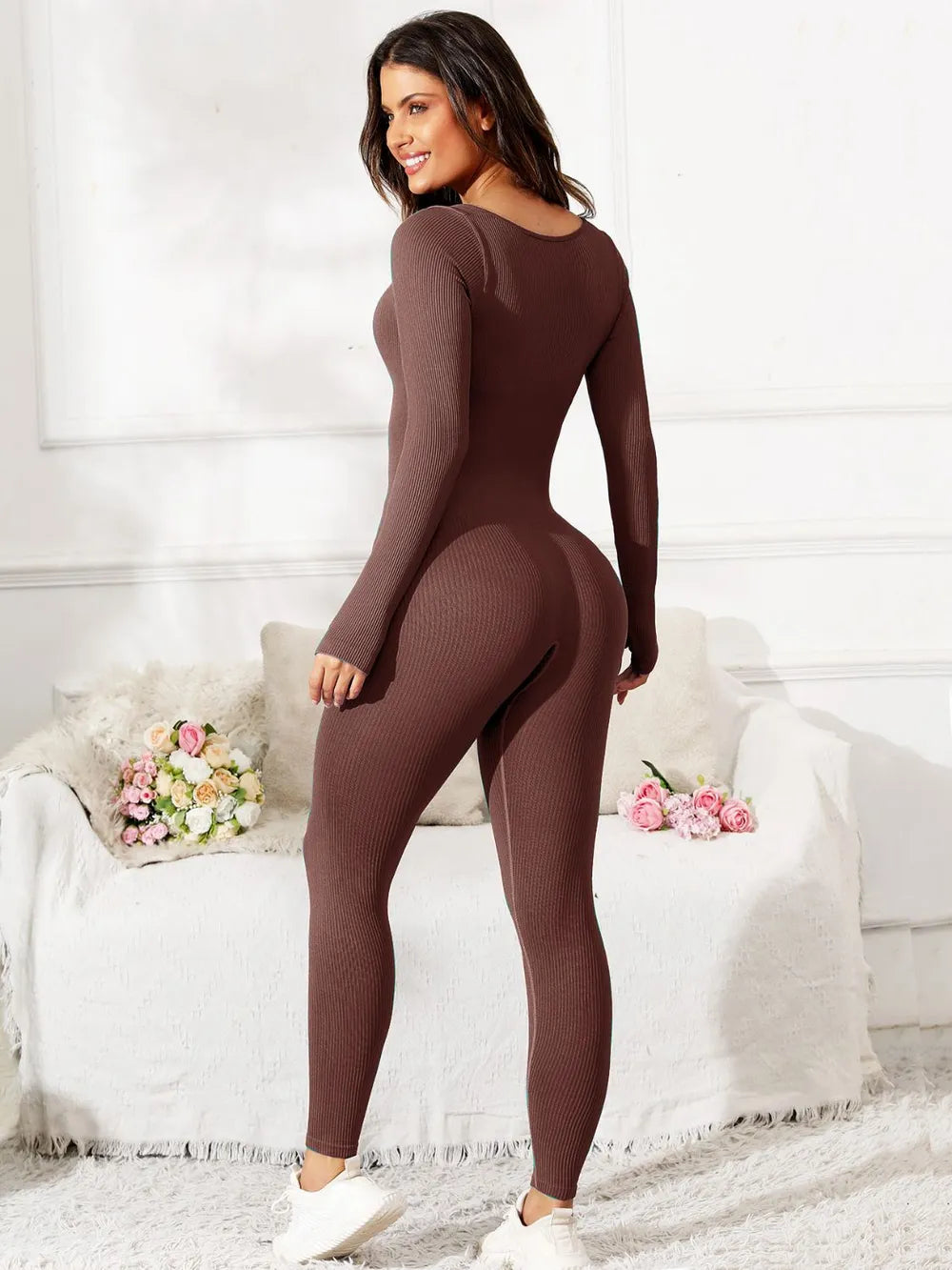 Woman wearing a brown bodysuit in a room with white walls and a white couch.