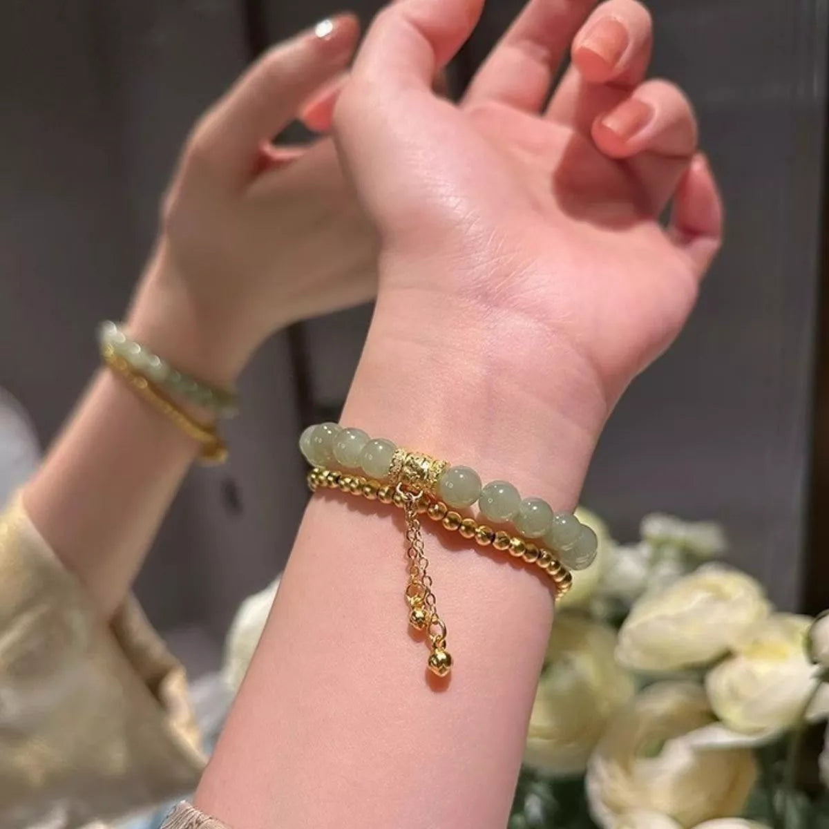 Close-up of a hand wearing a gold bracelet with green beads against a blurred background