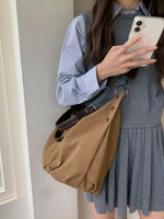Person holding a phone, wearing a gray dress and blue shirt, with a brown bag.