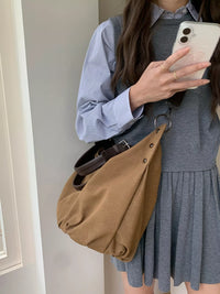 Person holding a phone, wearing a gray dress and blue shirt, with a brown bag.