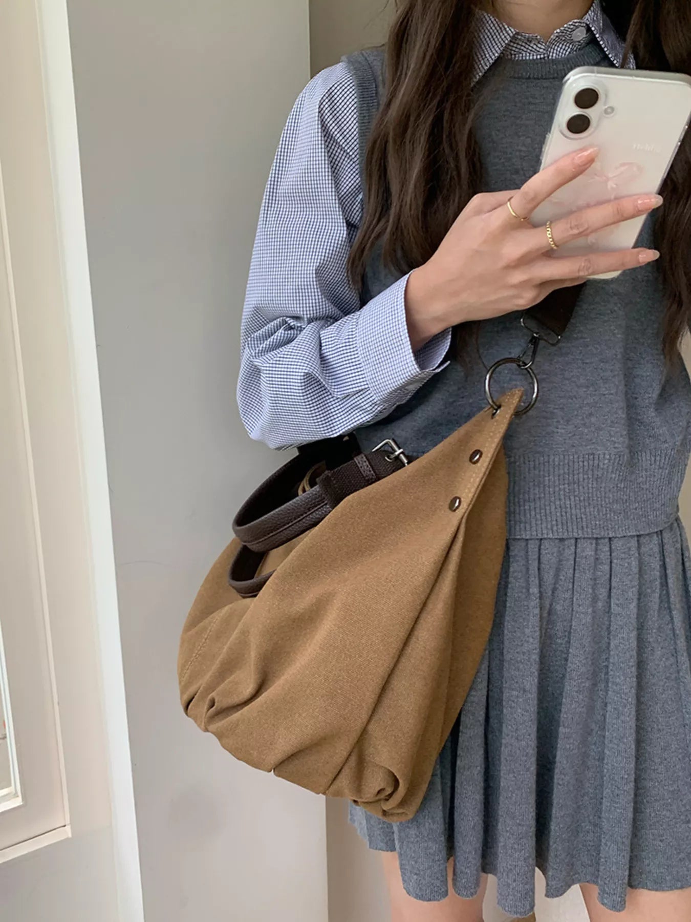 Person holding a phone, wearing a gray dress and blue shirt, with a brown bag.