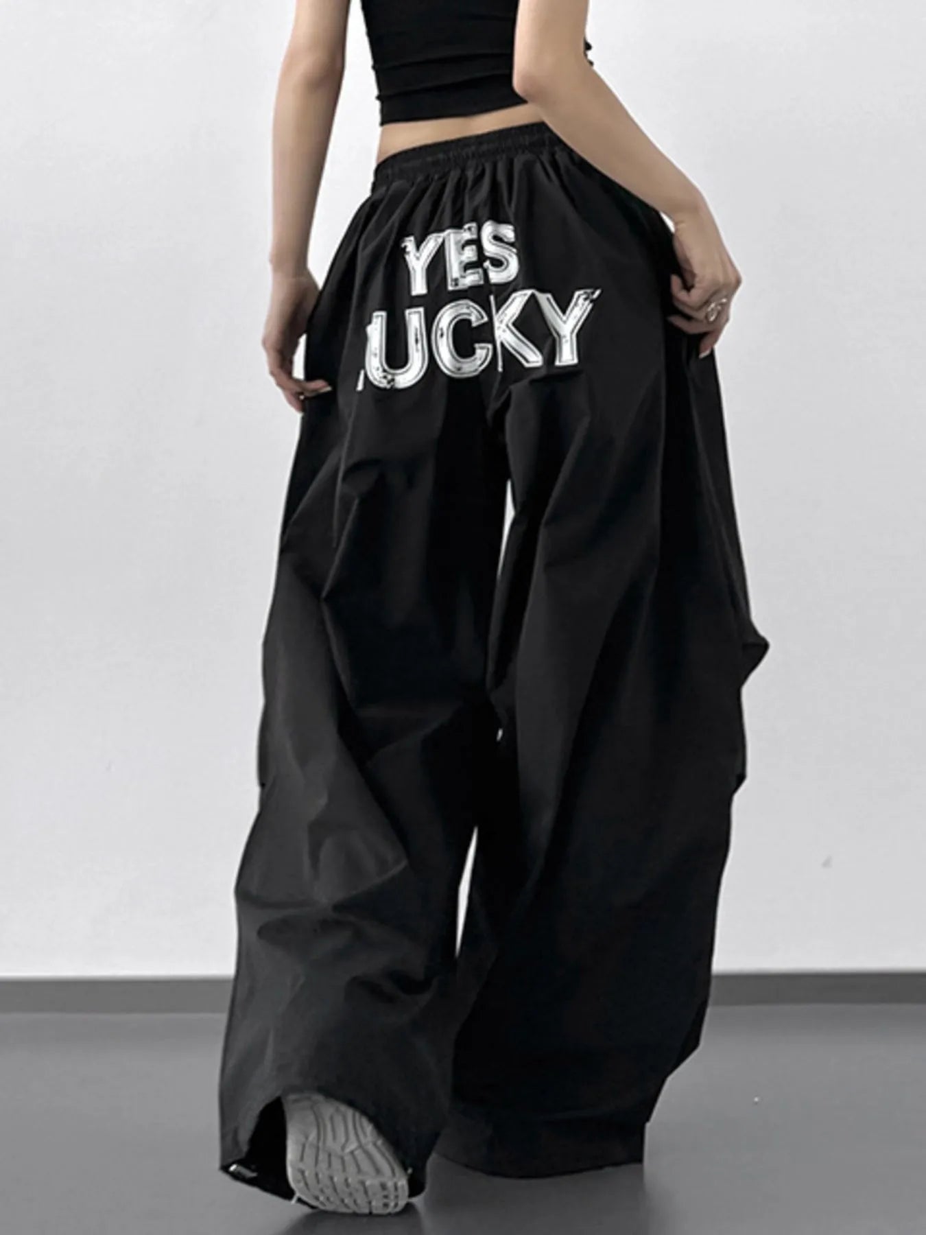 Person wearing black wide-leg pants with 'YES LUCKY' text on a plain background
