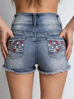 Blue denim shorts with star and stripe designs on the pockets against a neutral background