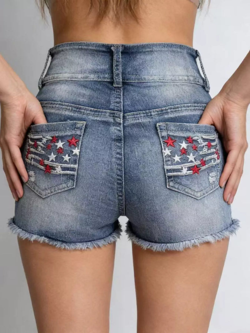 Blue denim shorts with star and stripe designs on the pockets against a neutral background