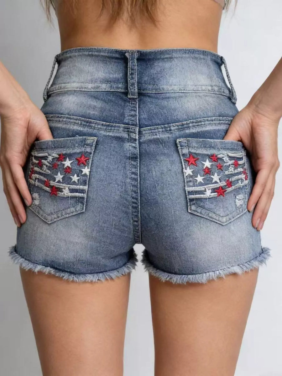 Blue denim shorts with star and stripe designs on the pockets against a neutral background