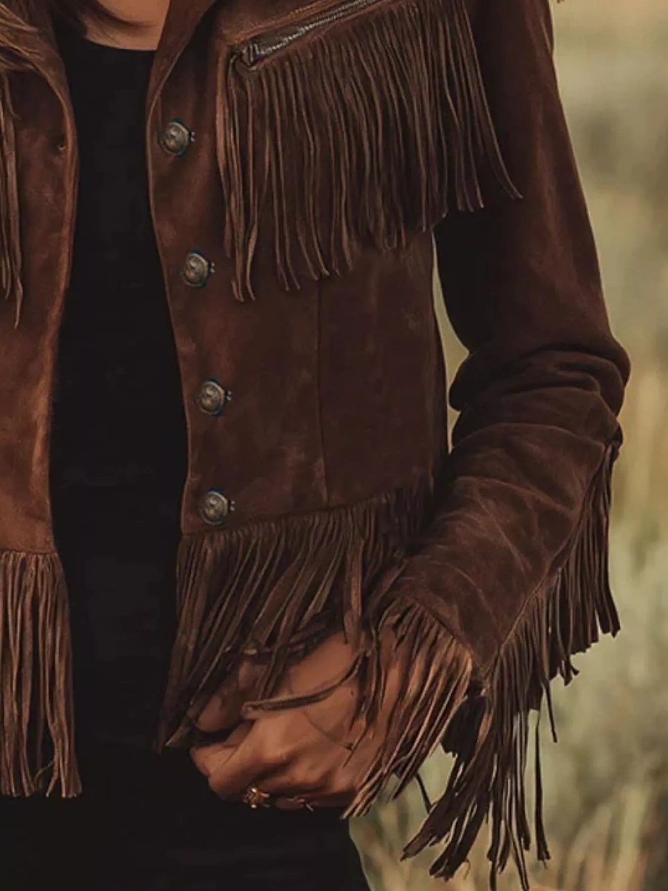 Brown suede jacket with fringes on a blurred natural background