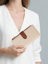 Person holding a beige clutch with brown strap against a plain background