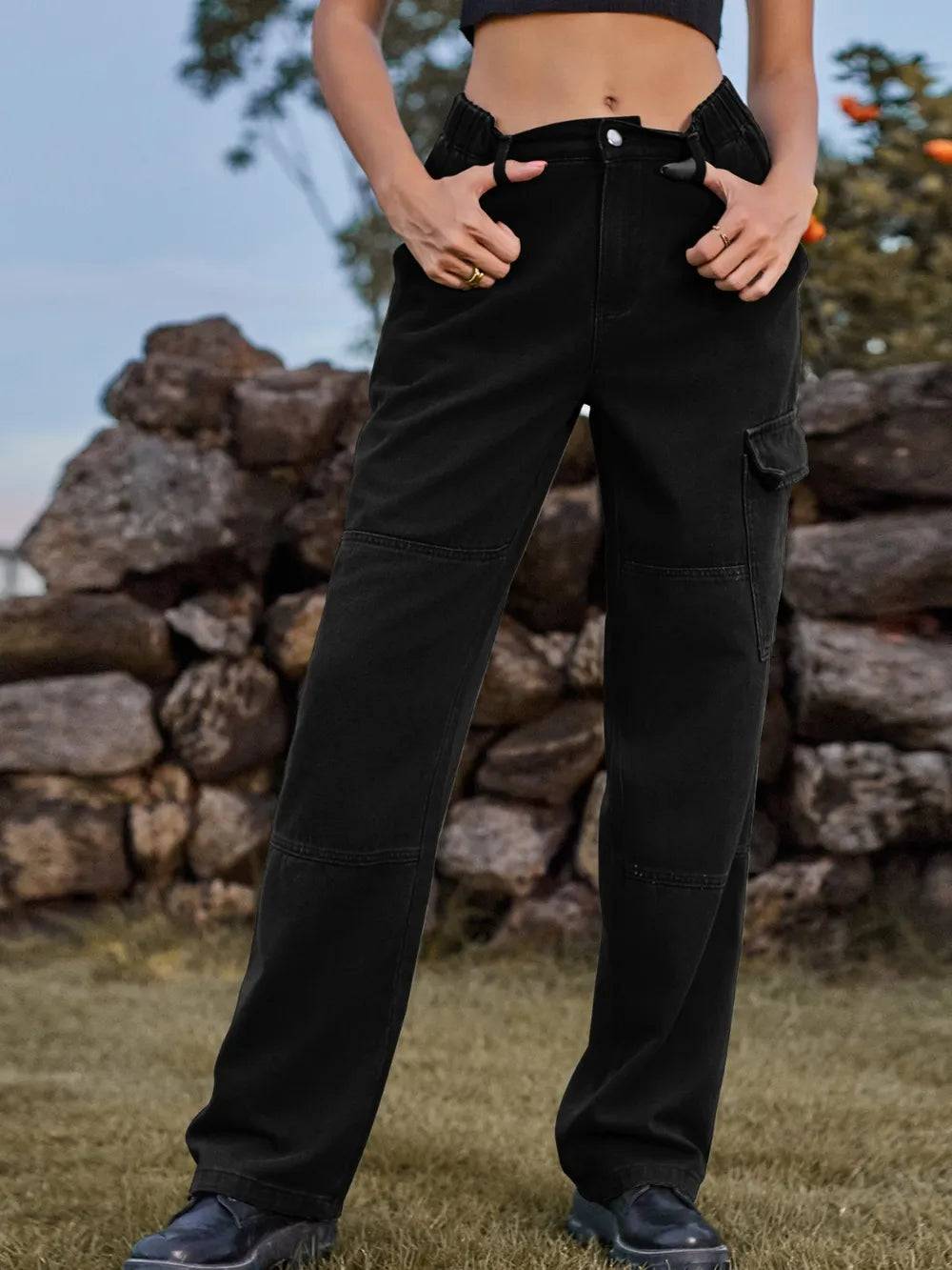 Person wearing black cargo pants standing in front of a stone wall.