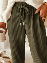 Person wearing olive green ribbed pants with a white sweater and beige background