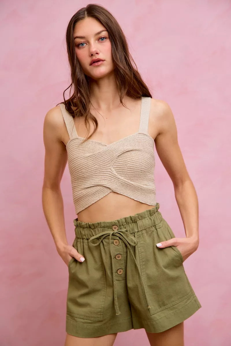 Woman wearing a beige knitted top and green shorts against a pink background