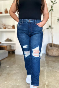Person wearing blue jeans with a black top in a room with shelves and plants.