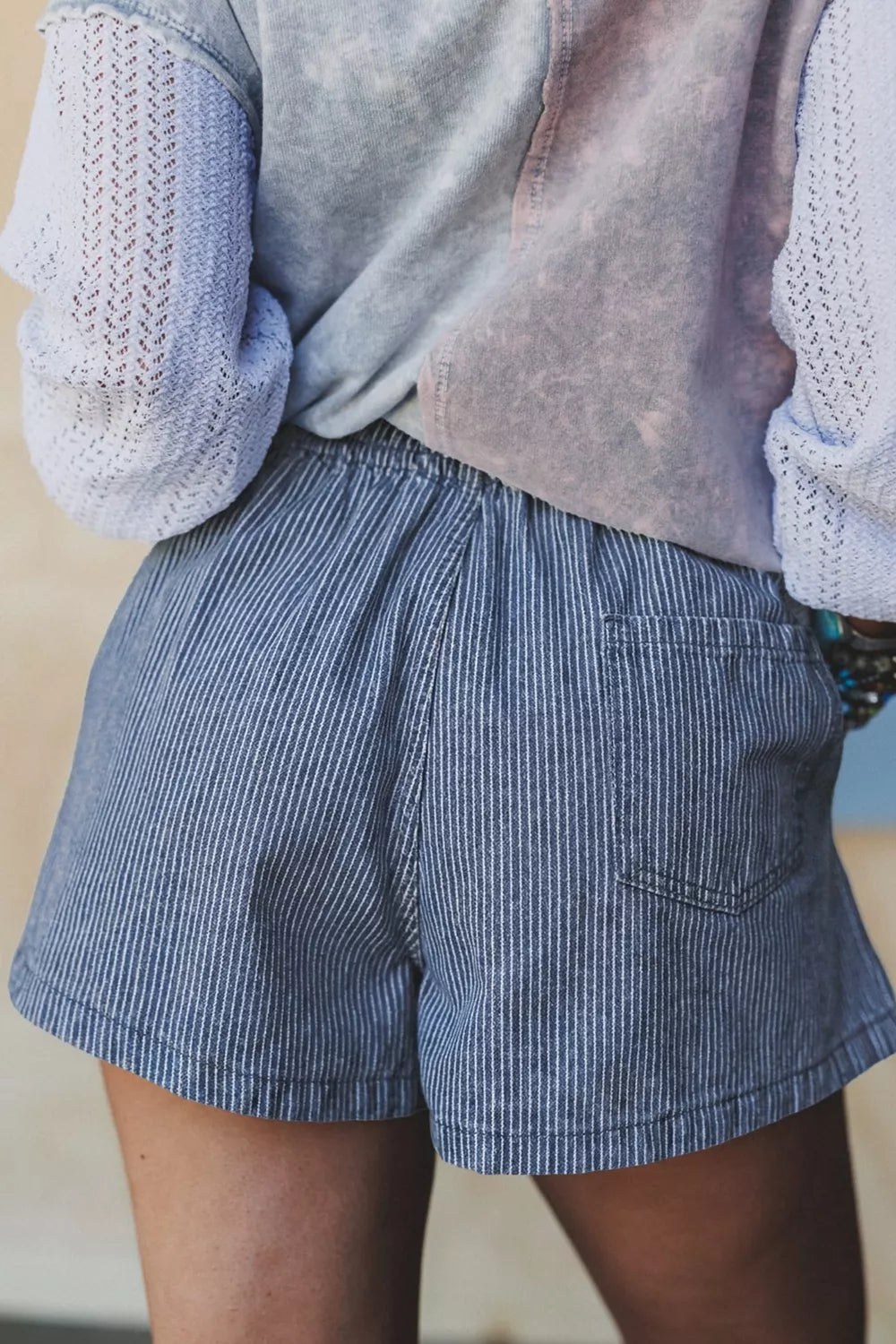 Person wearing blue striped shorts with a light sweater and vest.