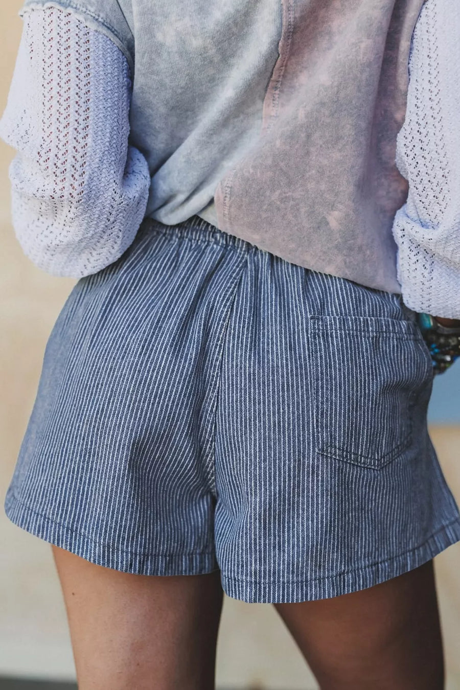 Person wearing blue striped shorts with a light sweater and vest.