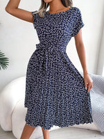 Woman wearing a navy blue floral dress sitting on a white couch.