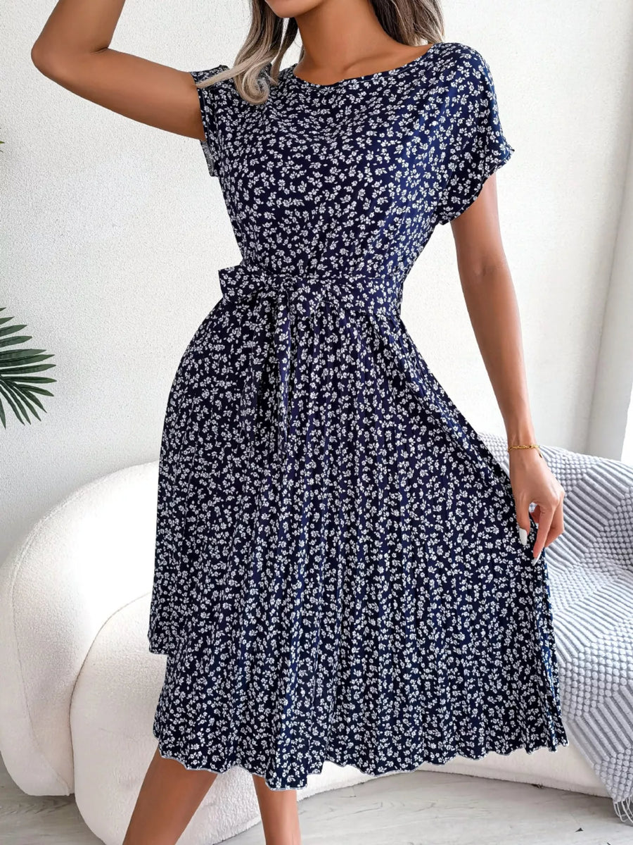 Woman wearing a navy blue floral dress sitting on a white couch.