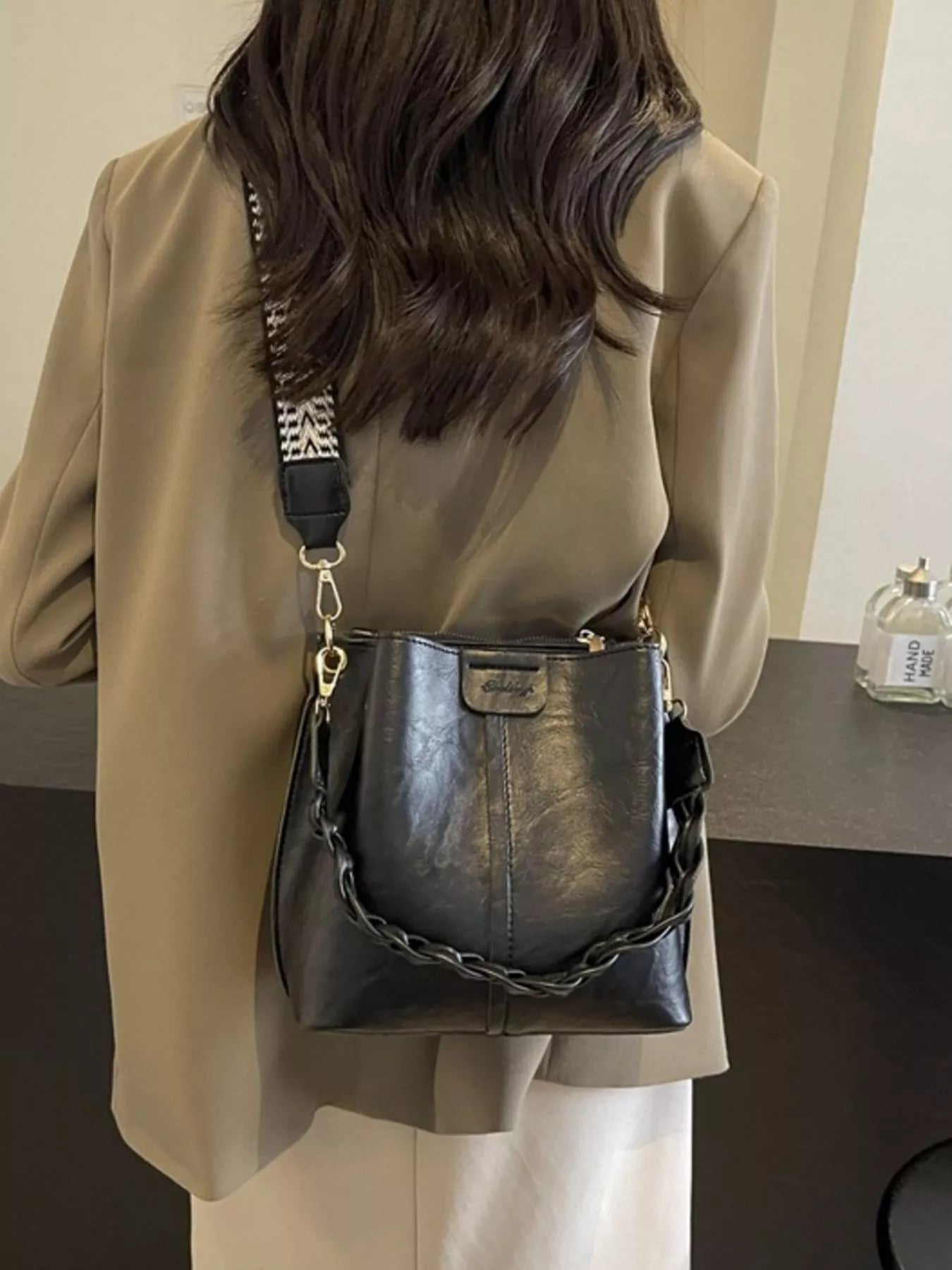 Person wearing a beige coat with a black leather handbag featuring a chain detail.