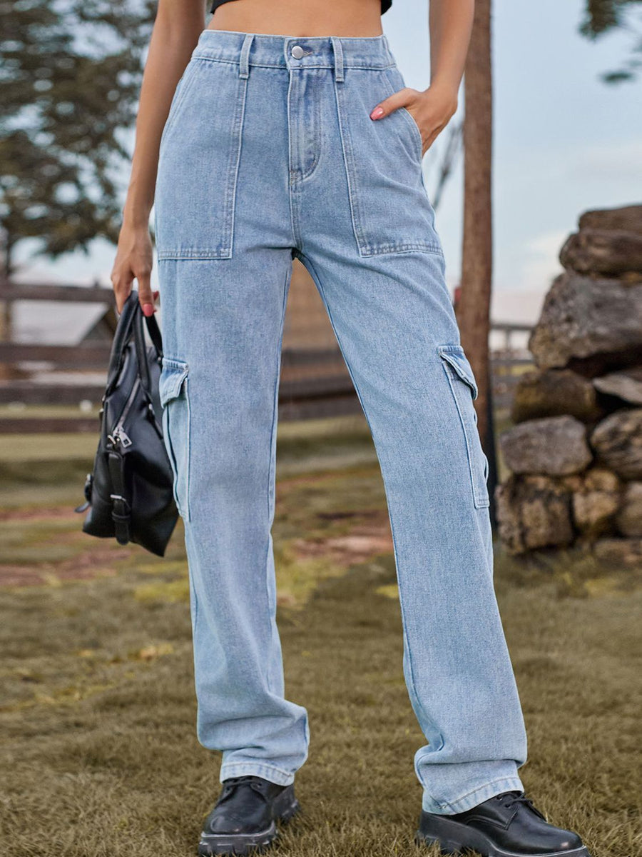 Person wearing light blue cargo pants standing outdoors with a wooden fence and stacked logs in the background.