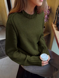 Person wearing a green sweater holding a coffee cup indoors.