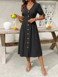 Woman in a black dress standing in front of a wooden table with fruits.