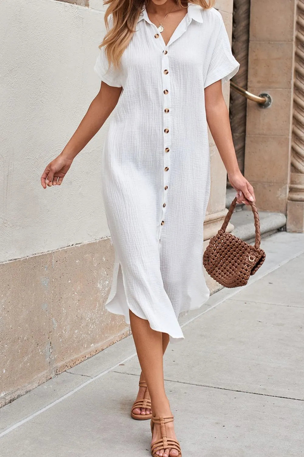 Woman wearing a white button-up dress with a brown woven handbag on a sidewalk.