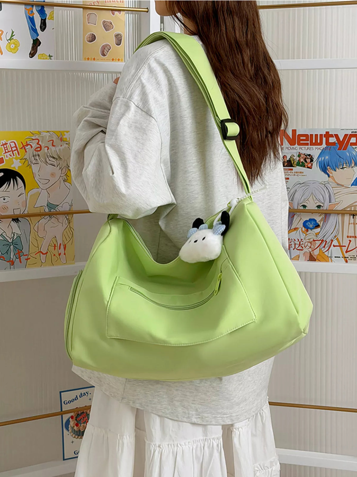 Person carrying a light green bag with a small plush toy attached, in front of a shelf with various items.