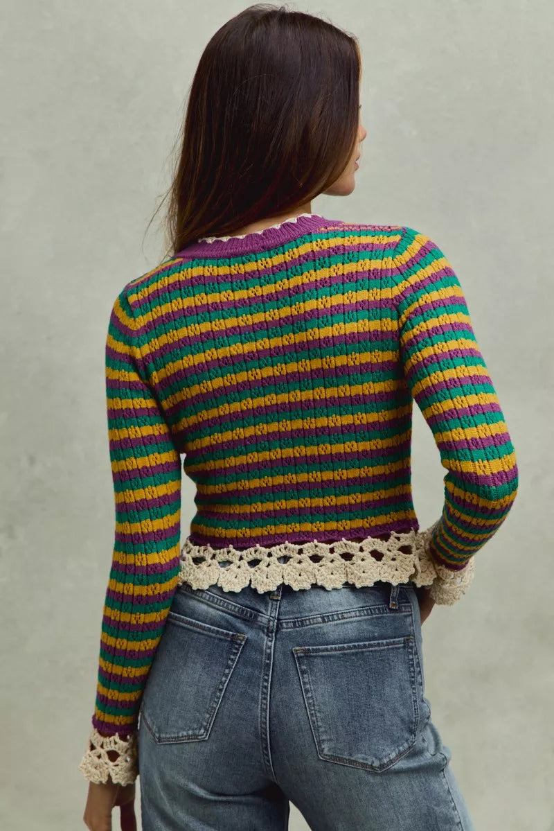 Person wearing a colorful striped sweater with lace trim against a plain background