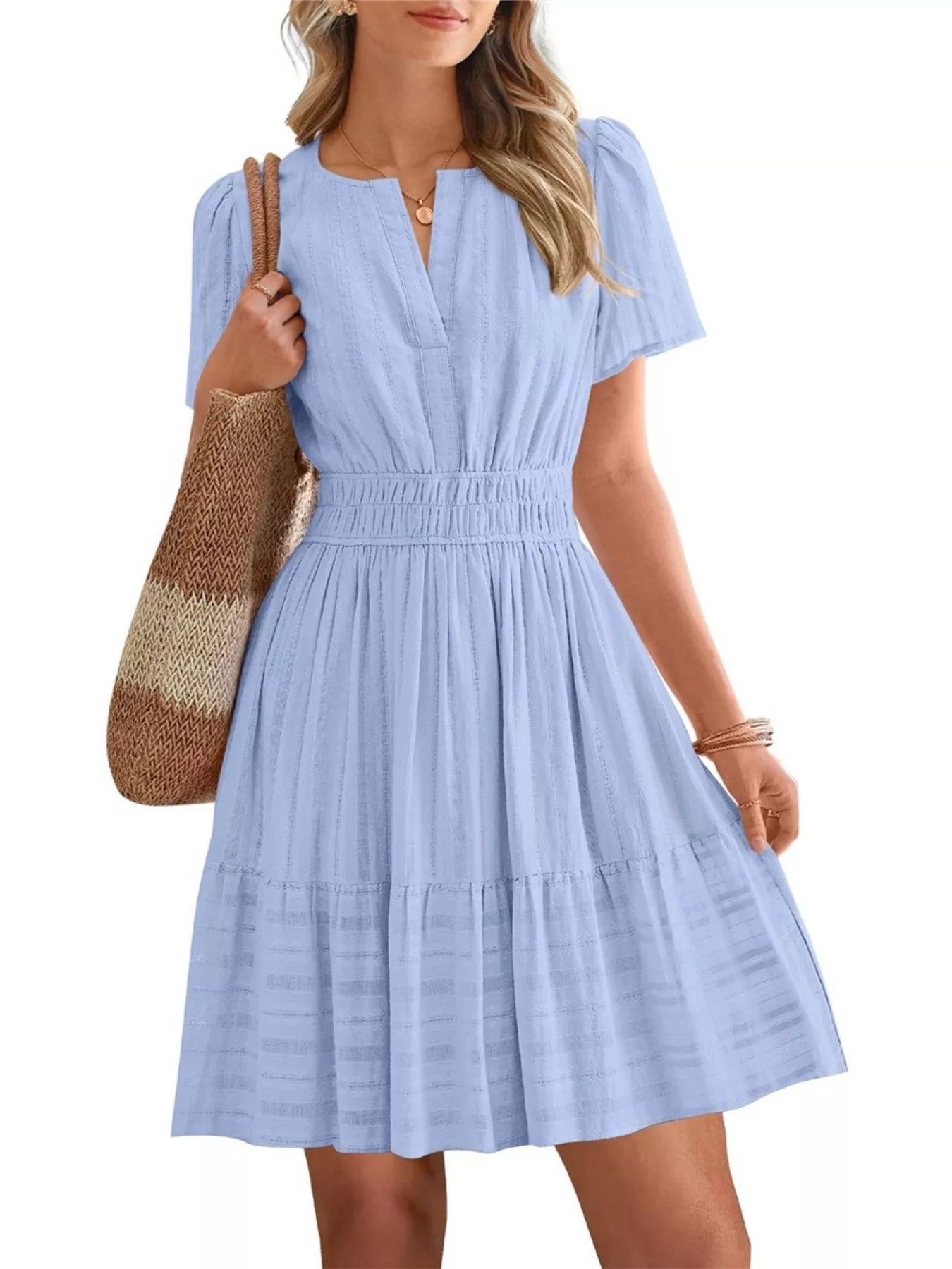 Woman wearing a light blue dress holding a brown bag on a white background