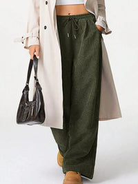 Person wearing green wide-leg pants, a beige trench coat, and brown shoes on a white background