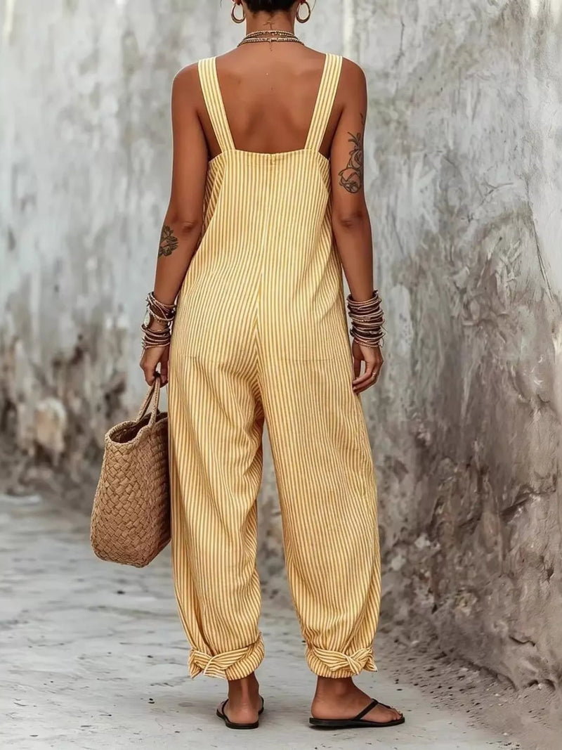 Person wearing a yellow striped jumpsuit holding a woven bag against a textured wall.