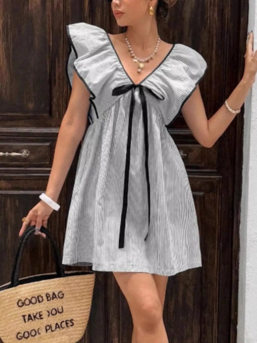 Woman wearing a gray dress with black accents, holding a straw bag with text, against a wooden background.