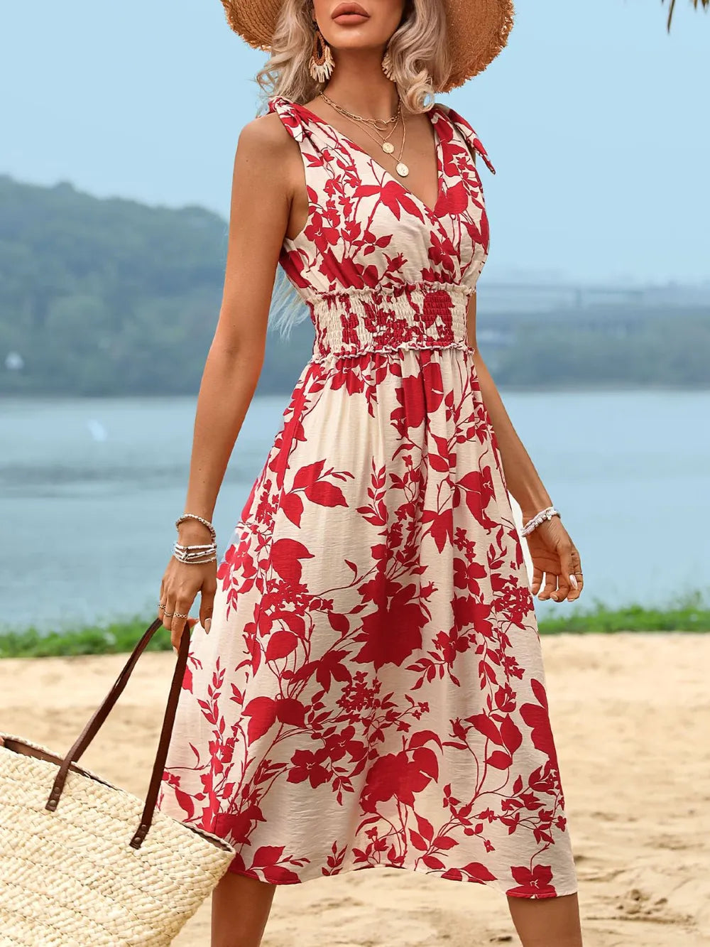 Woman in a red and white floral dress standing on a beach with a blurred background