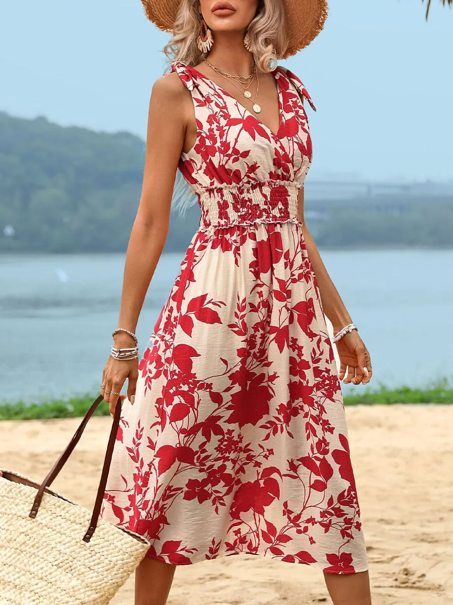 Woman in a red and white floral dress standing on a beach with a blurred background
