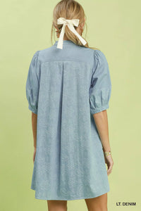 Light denim dress worn by a person with a white bow in their hair on a light green background