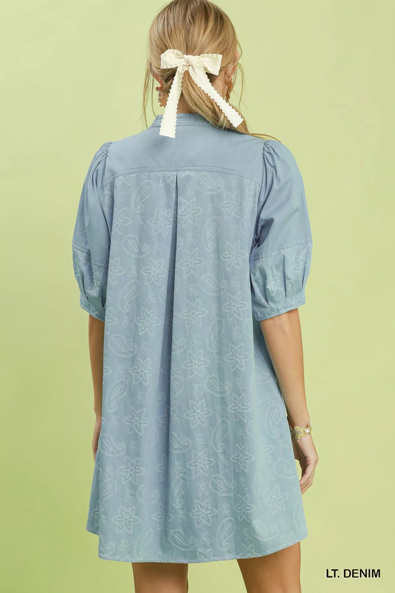Light denim dress worn by a person with a white bow in their hair on a light green background
