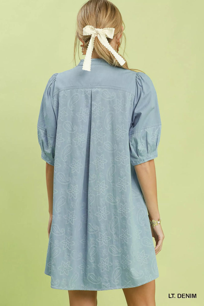 Light denim dress worn by a person with a white bow in their hair on a light green background