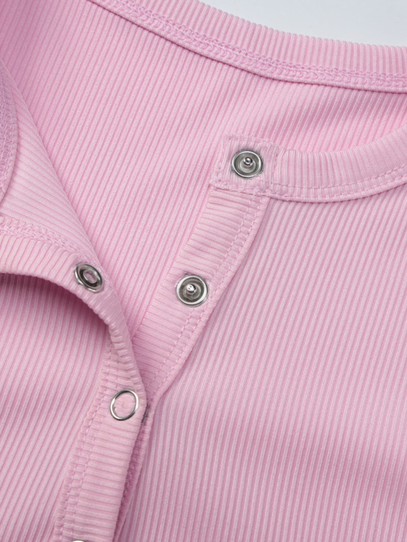 Close-up of a pink ribbed garment with buttons on a light gray background