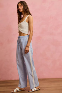 Woman wearing a white top and light blue pants with a pink background
