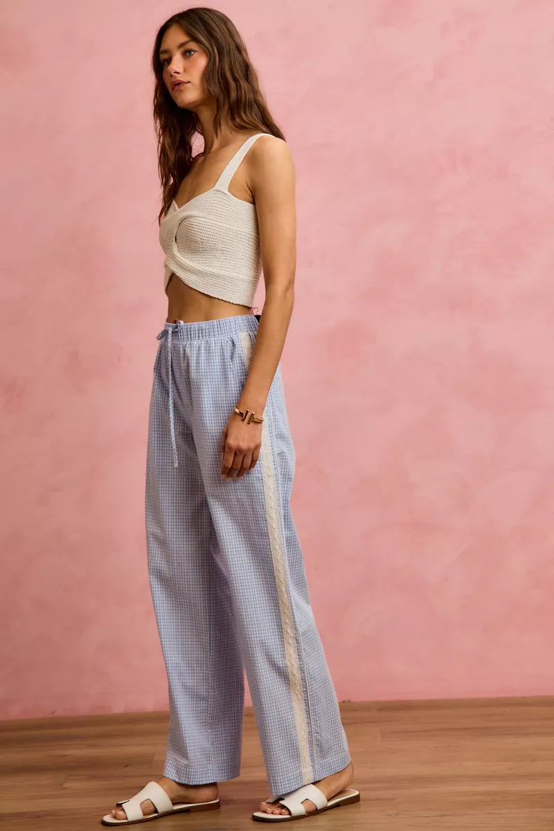 Woman wearing a white top and light blue pants with a pink background