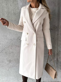 Woman wearing a beige coat holding a matching handbag against a gray background