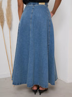 Person wearing a long blue denim skirt with a white background