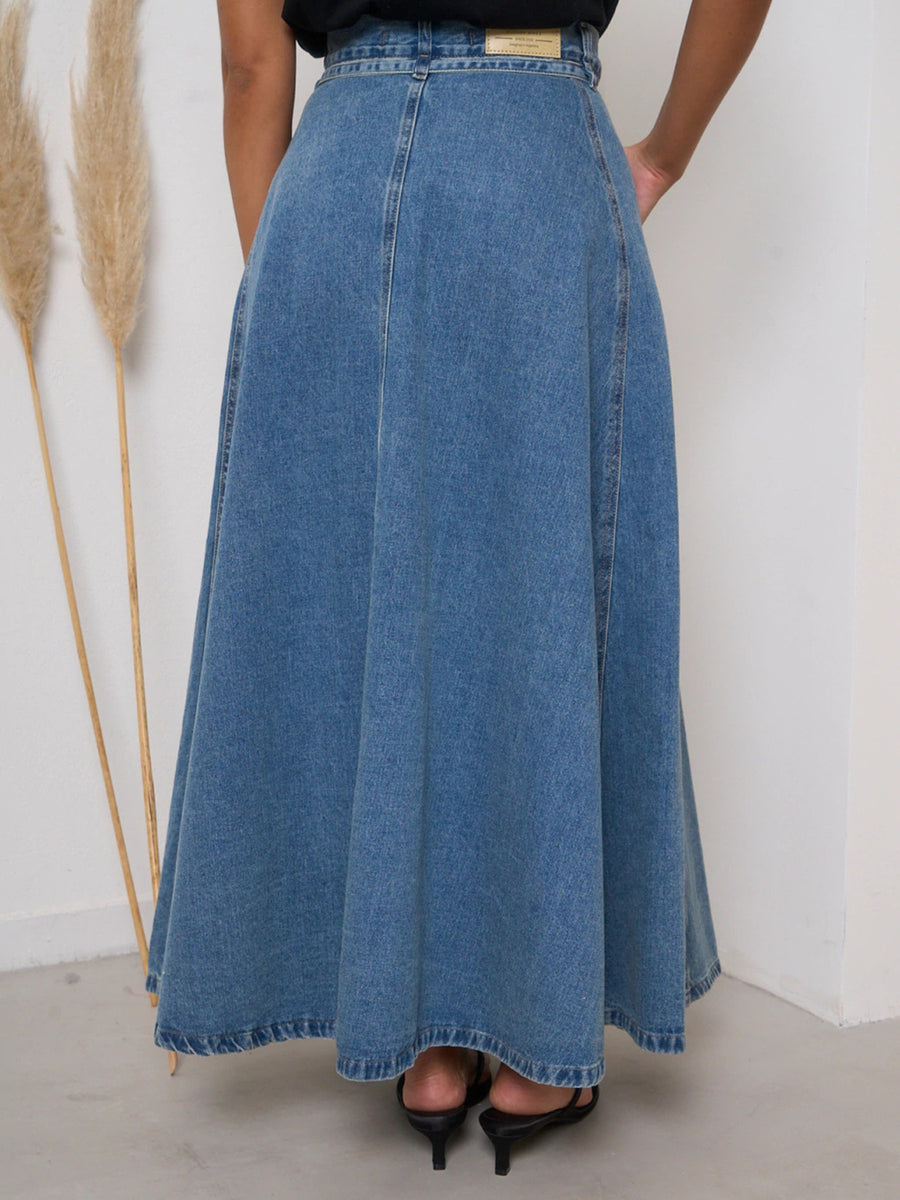 Person wearing a long blue denim skirt with a white background