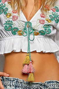 Close-up of a person wearing a white blouse with colorful embroidery and a decorative belt with tassels.