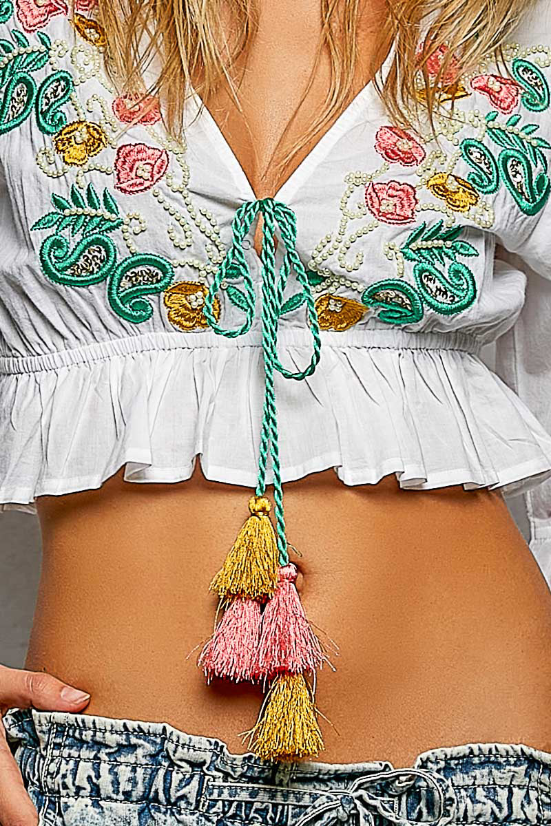 Close-up of a person wearing a white blouse with colorful embroidery and a decorative belt with tassels.
