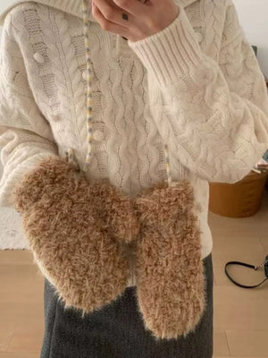Person wearing a white cable knit sweater and brown fuzzy gloves indoors.