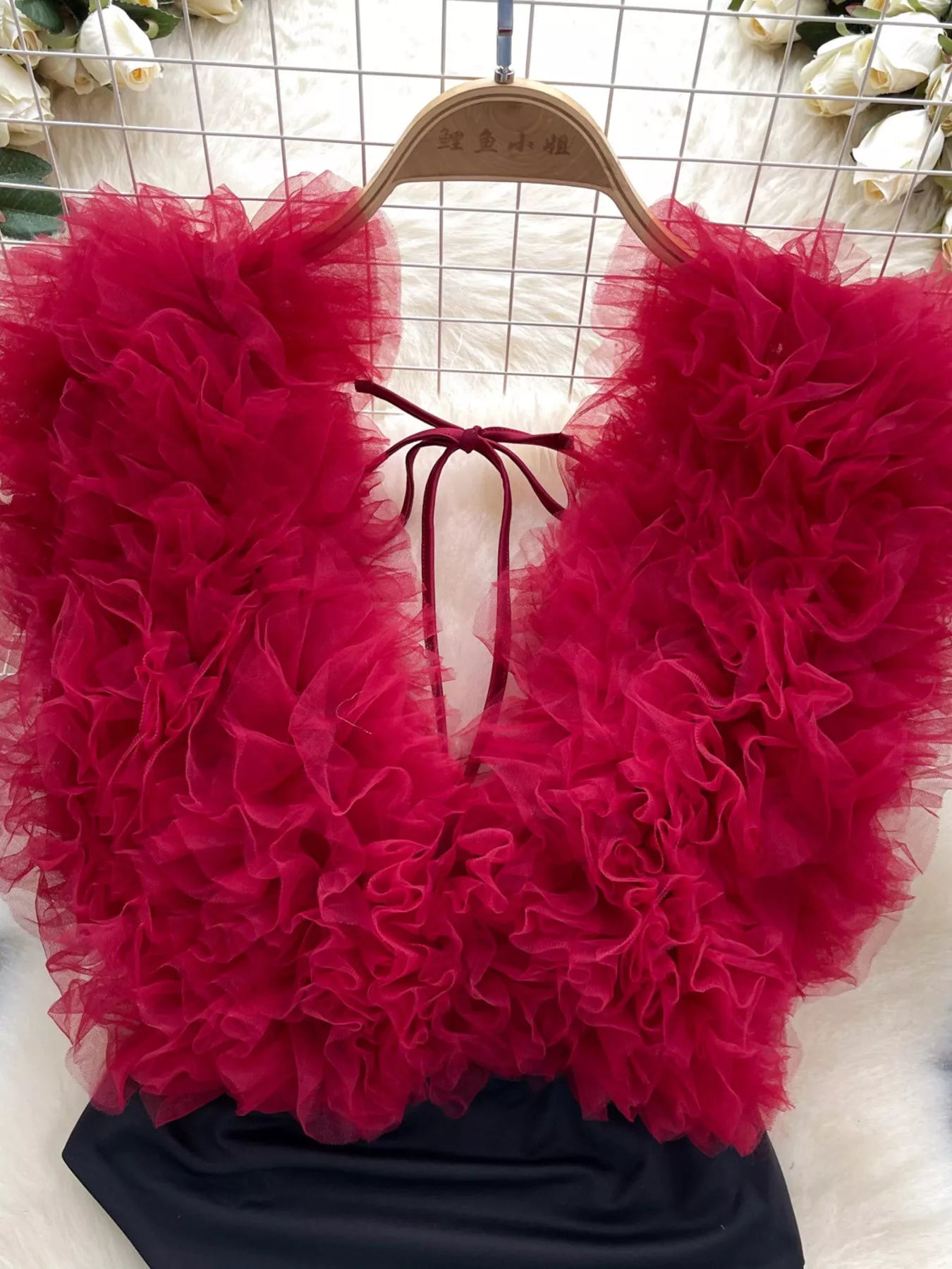 Red ruffled top on a hanger with a white floral background