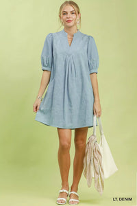 Woman wearing a light blue dress holding a beige bag on a light green background